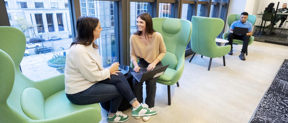 two women sitting in chairs in a room with large windows