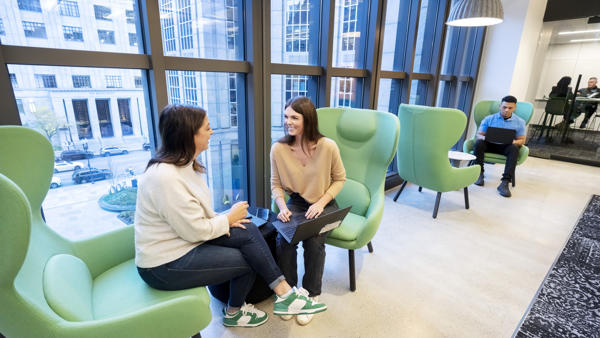 two women sitting in chairs in a room with large windows