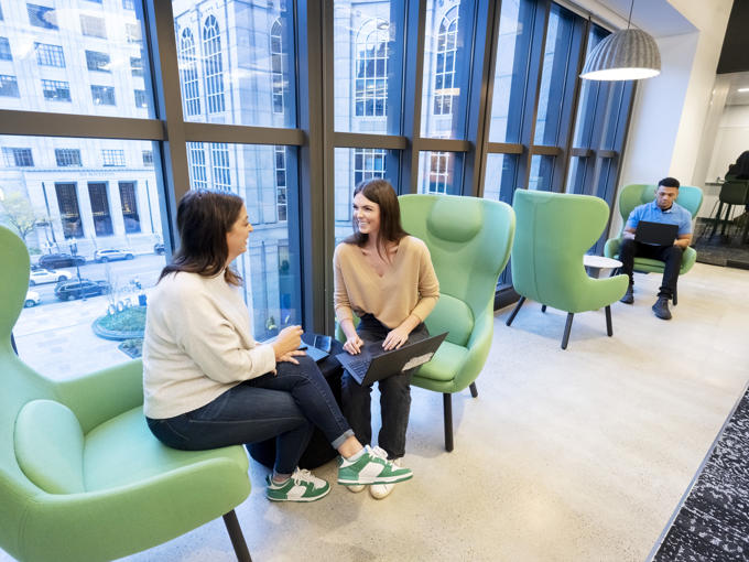 two women sitting in chairs in a room with large windows