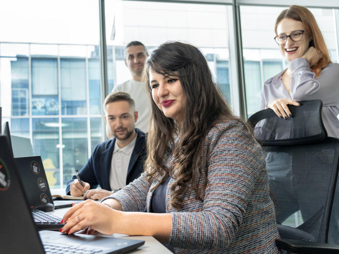 a woman sitting at a desk with a laptop and a group of people behind her