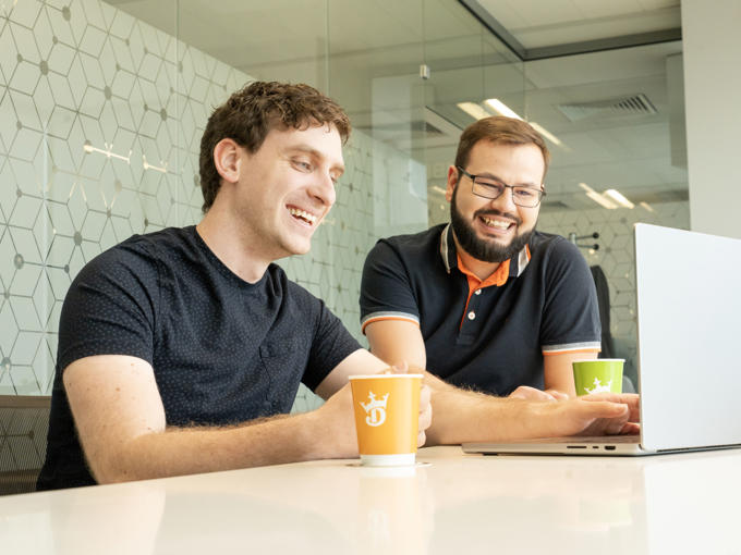 two men sitting at a table looking at a laptop