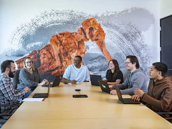 a group of people sitting around a table with laptops