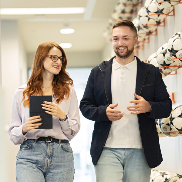 a man and woman walking in a hallway with football balls
